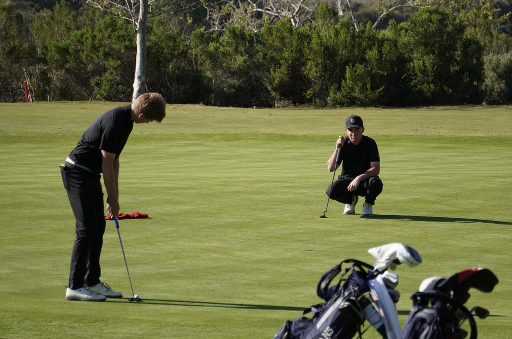 Gavin Heller on the putting green of hole 1 with teammate Liam McNamara helping line up the putt.
